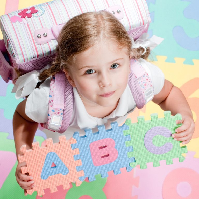 Ein Mädchen mit Schulmappe zeigt das ABC.