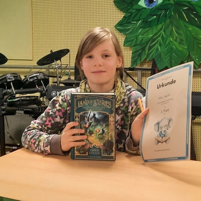 Helene sitzt am Tisch und präsentiert
ihr vorgestelltes Buch und ihre Urkunde.