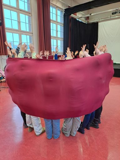 Kinder stehen gemeinsam in einem großen Tuch.