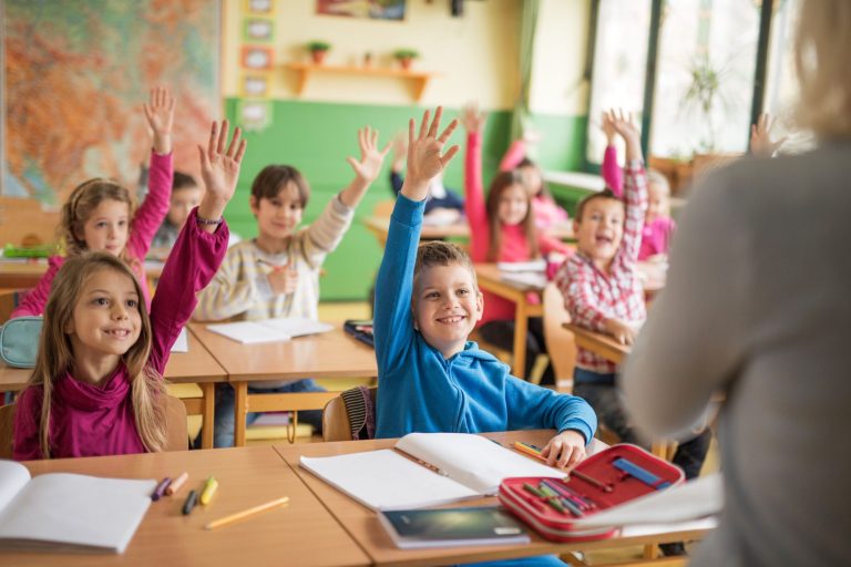 Viele Kinder sitzen im Klassenraum und melden sich.